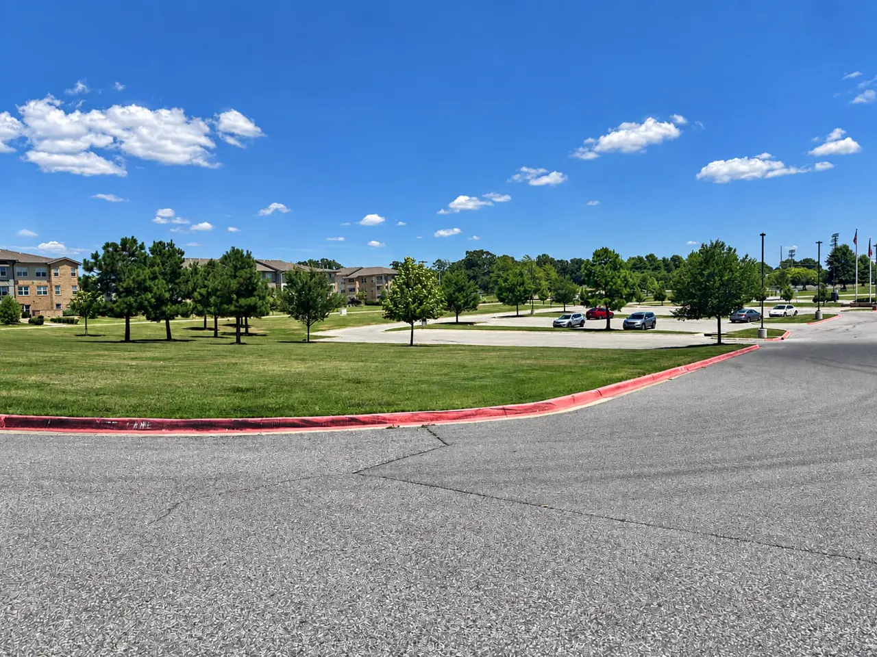Wide mown lawn with young shade trees between an apartment building and a parking lot