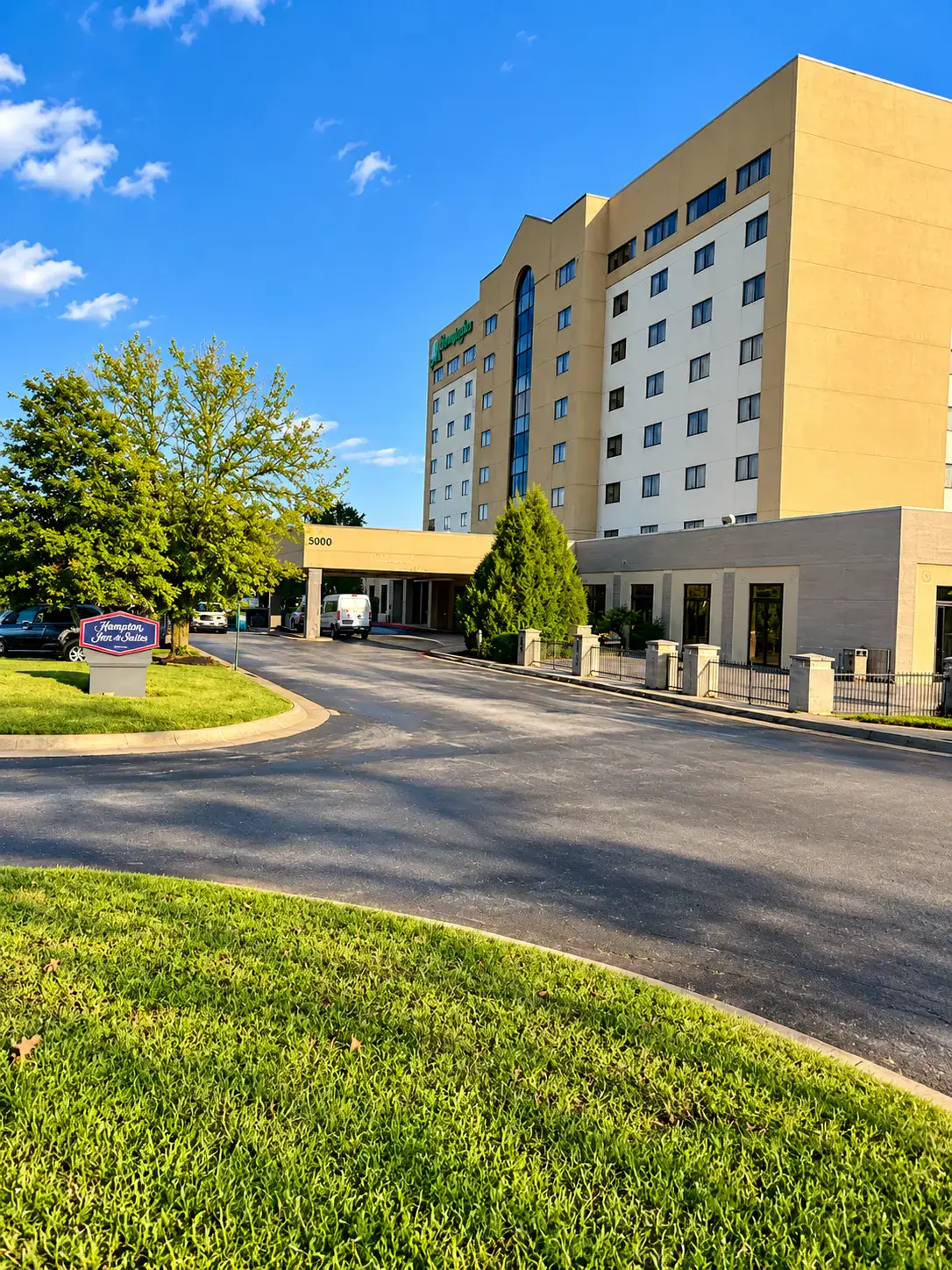 Mown lawn and trimmed trees beside the entrance drive of a multi-storey hotel