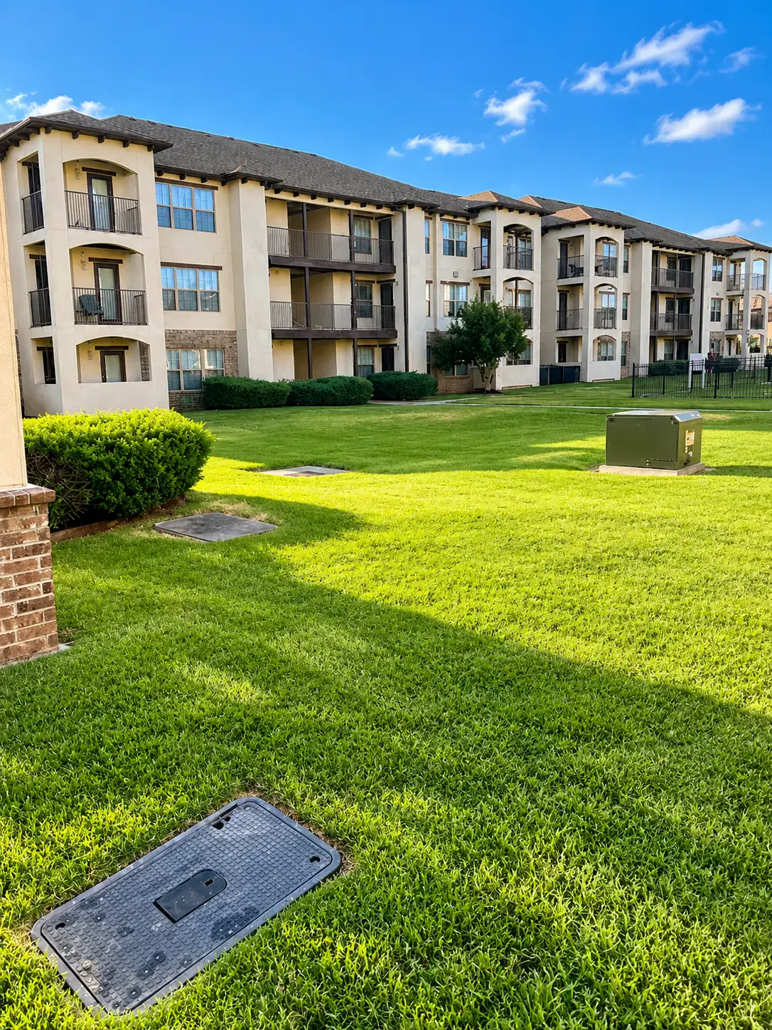 Large mown lawn in front of three-storey apartment buildings with clipped shrubs at the foundations